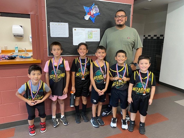 A group of young basketball players with medals and their coach inside a building.