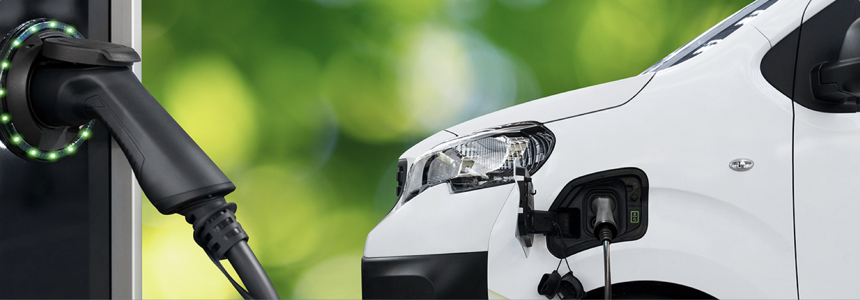An electric vehicle being charged at a charging station with a green, out-of-focus background.