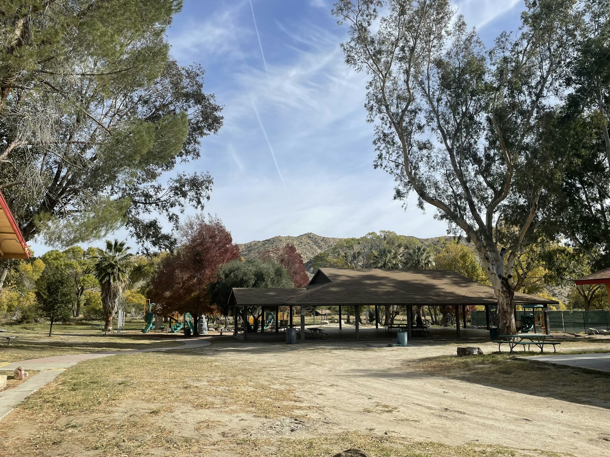 Park with picnic tables, trees, mountainside, and a clear sky.