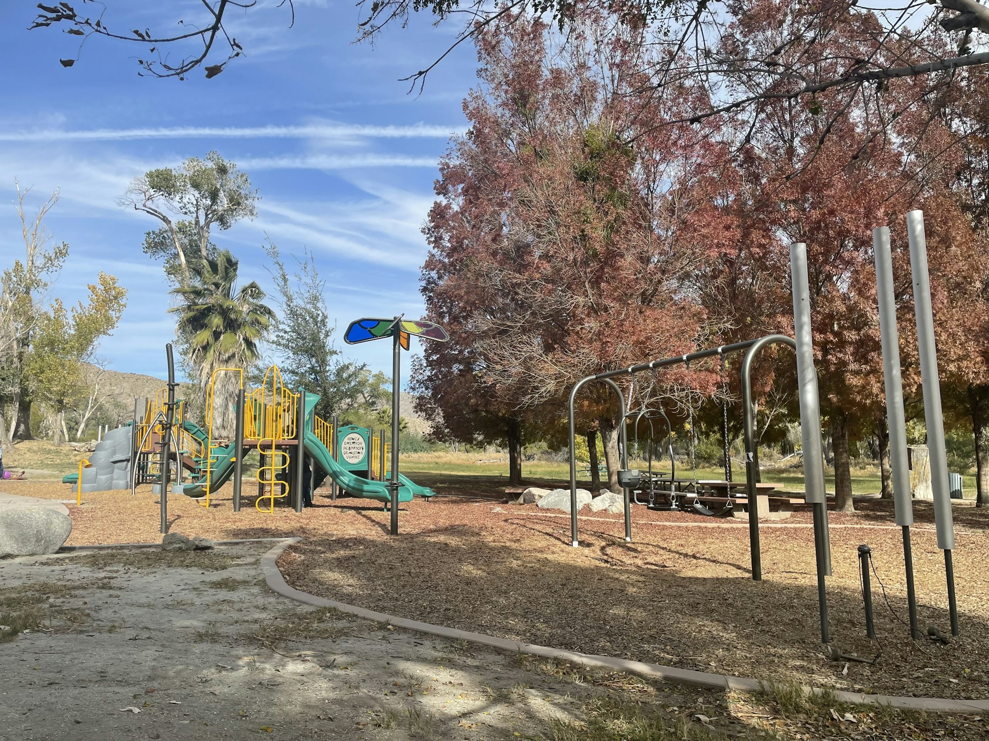 A playground with slides, swings, and colorful equipment surrounded by trees and blue skies.