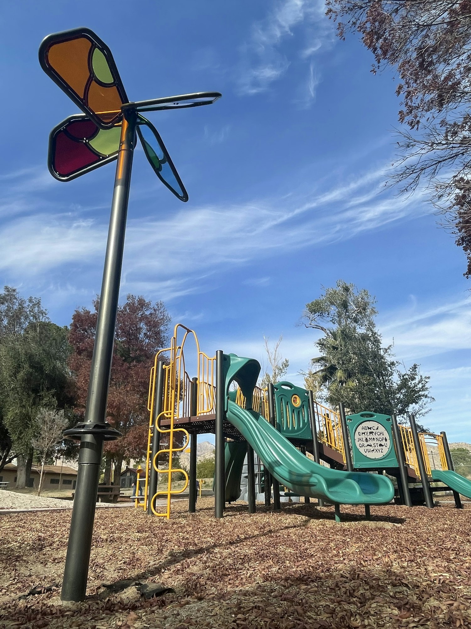 A playground with slides, climbing structures, and a whimsical butterfly sculpture against a blue sky with clouds.