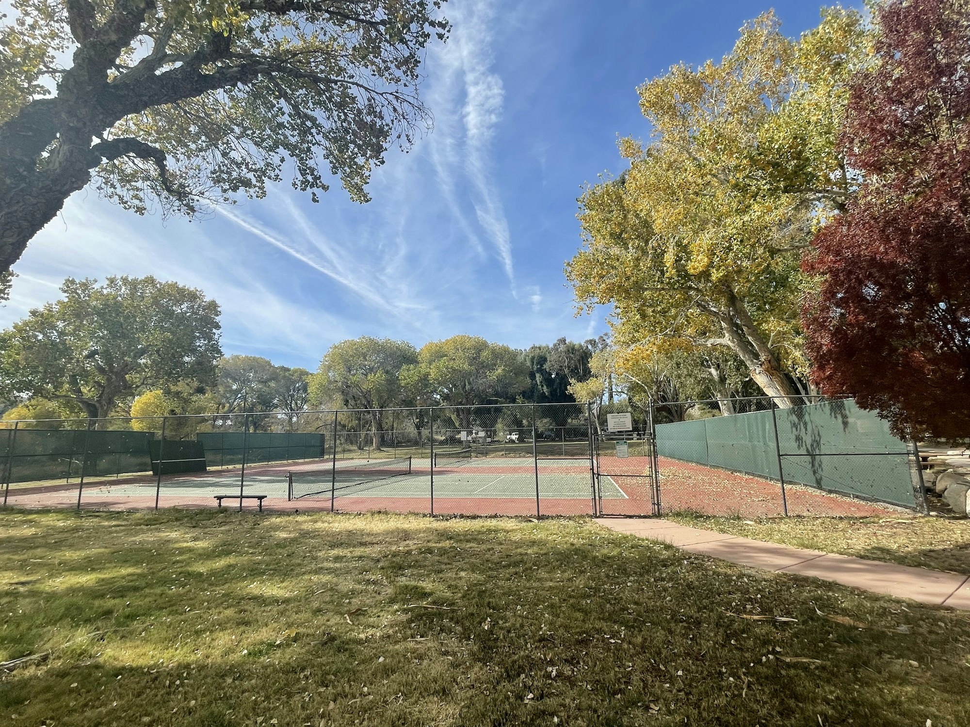 Tennis courts surrounded by trees with autumn foliage under a blue sky with wispy clouds.