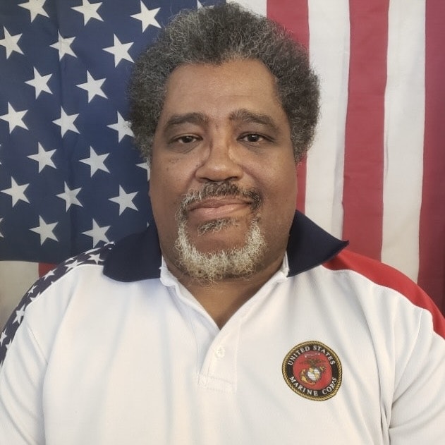 A person in a Marine Corps polo shirt, in front of an American flag.