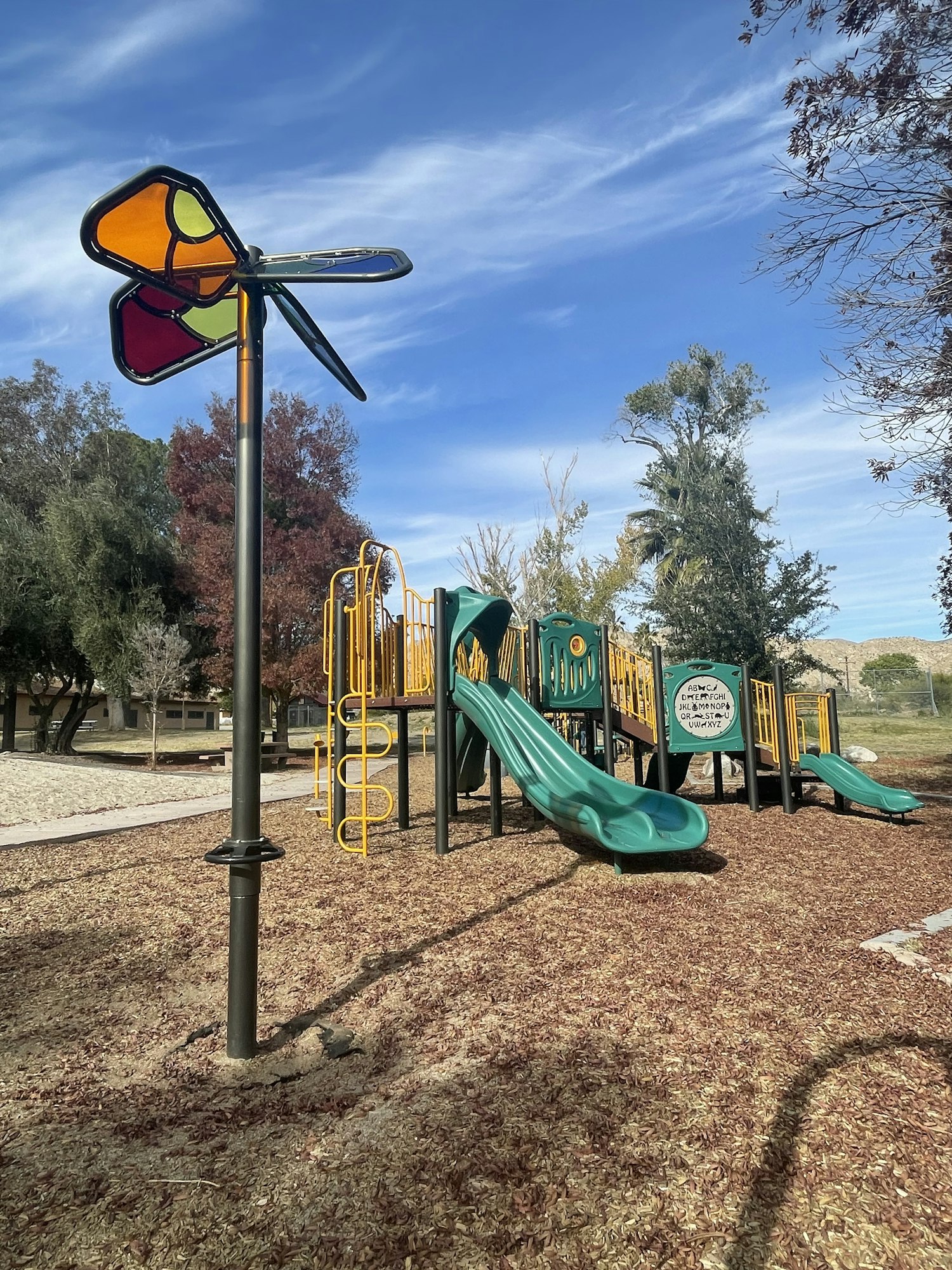 A colorful playground with slides and climbing structures, under a blue sky with wispy clouds. (Note: Image is rotated)