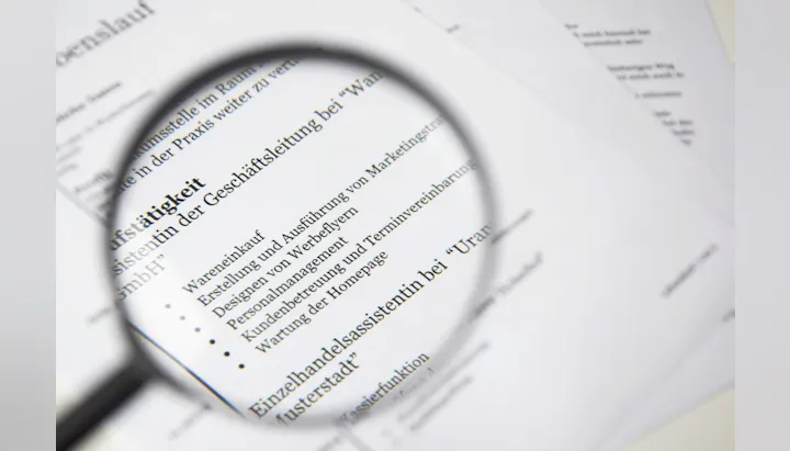 The image shows a resume or CV with various job roles and responsibilities, viewed through a magnifying glass.