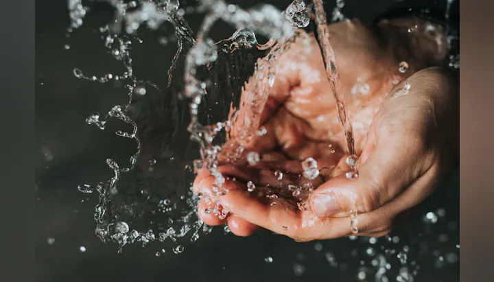 A pair of hands catching splashing water droplets against a dark background, creating a dynamic and fluid scene.