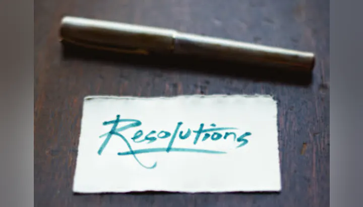 The image features a silver pen next to a note that says "Resolutions" in elegant, cursive handwriting.