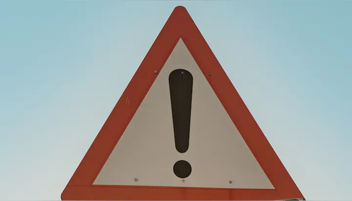 A large triangular warning sign featuring an exclamation mark against a blue sky background.