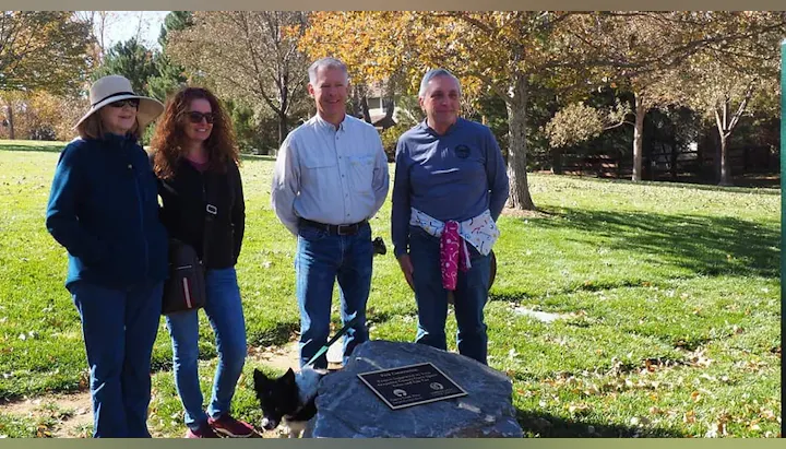 A group of four people, standing together by a commemorative plaque on a sunny day in a park.