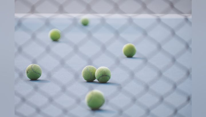 Tennis balls scattered on a court, viewed through a chain-link fence.