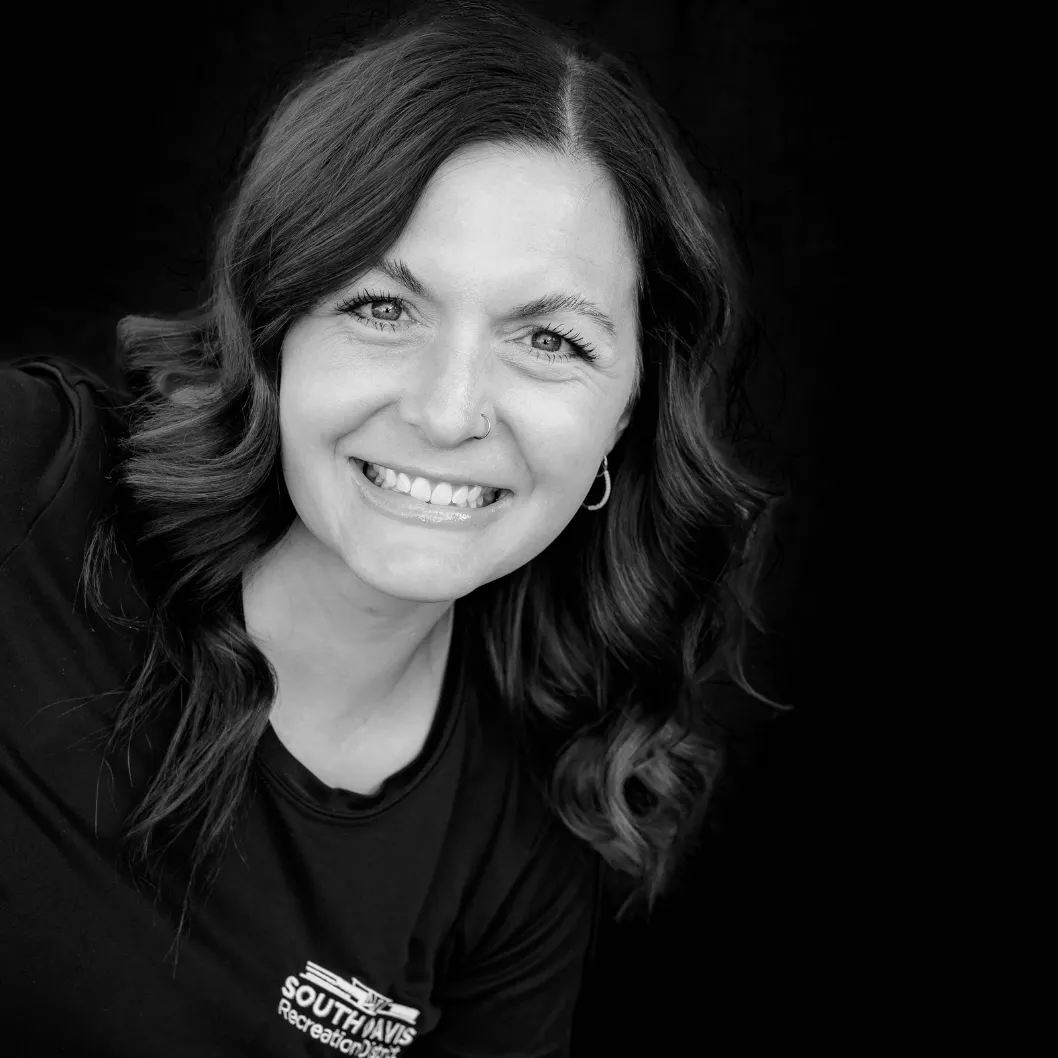 A smiling woman with wavy hair, wearing a "South Paws Recreation" black shirt, in a black-and-white portrait.