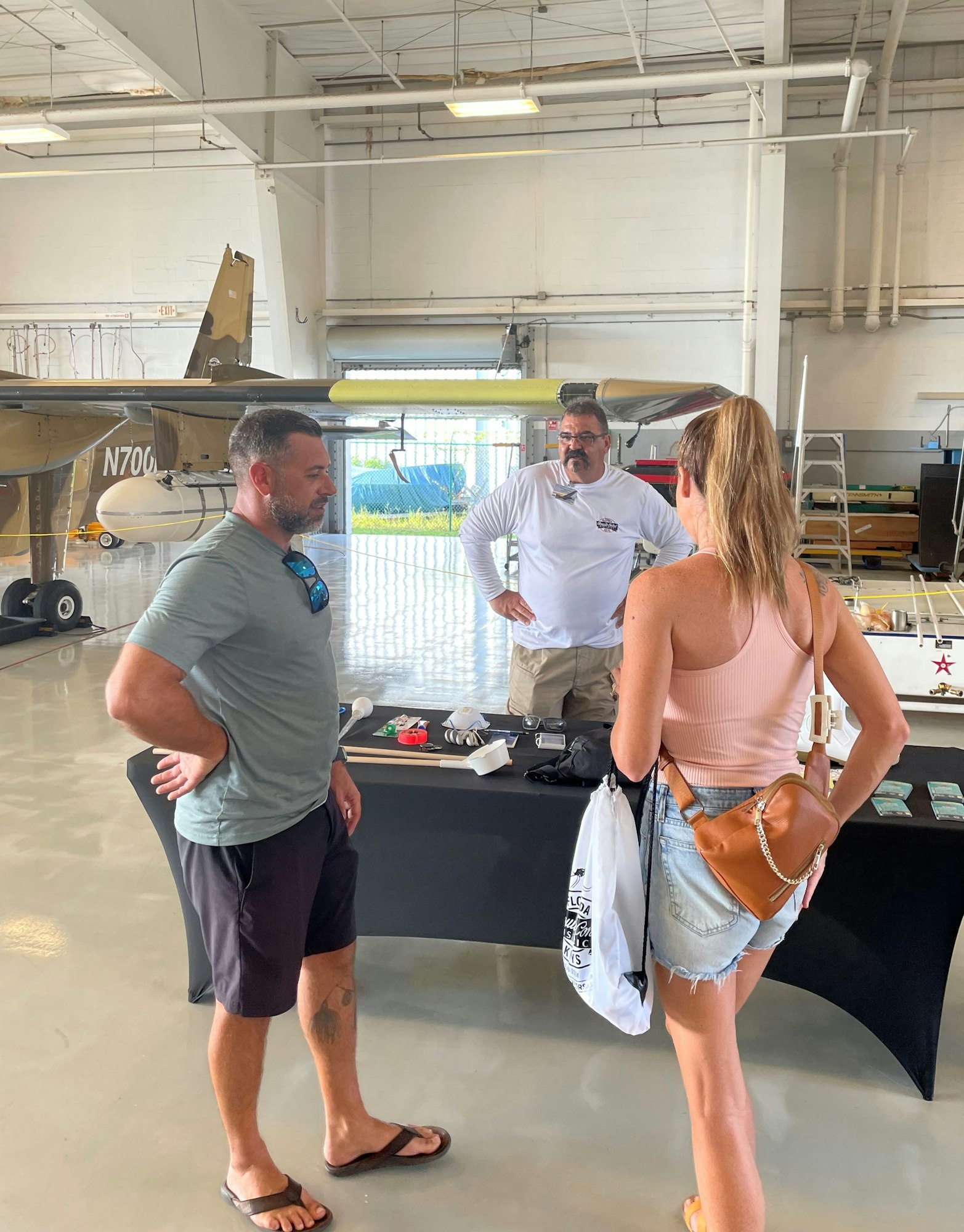 Three people conversing near a table in an aircraft hangar.