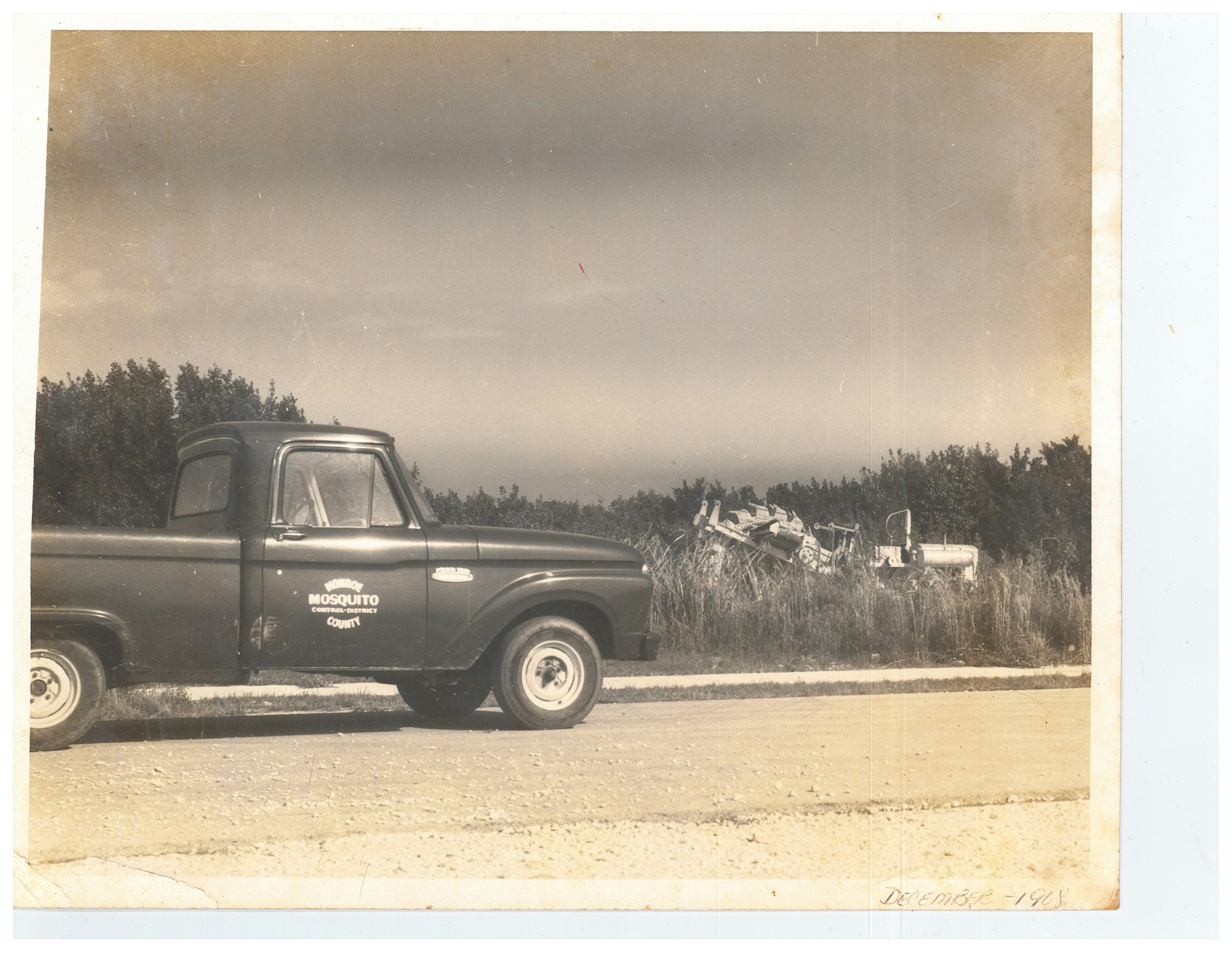 Vintage truck labeled "MOSQUITO Control District" on a rural road, with tall grass and bushes, dated December 1968.