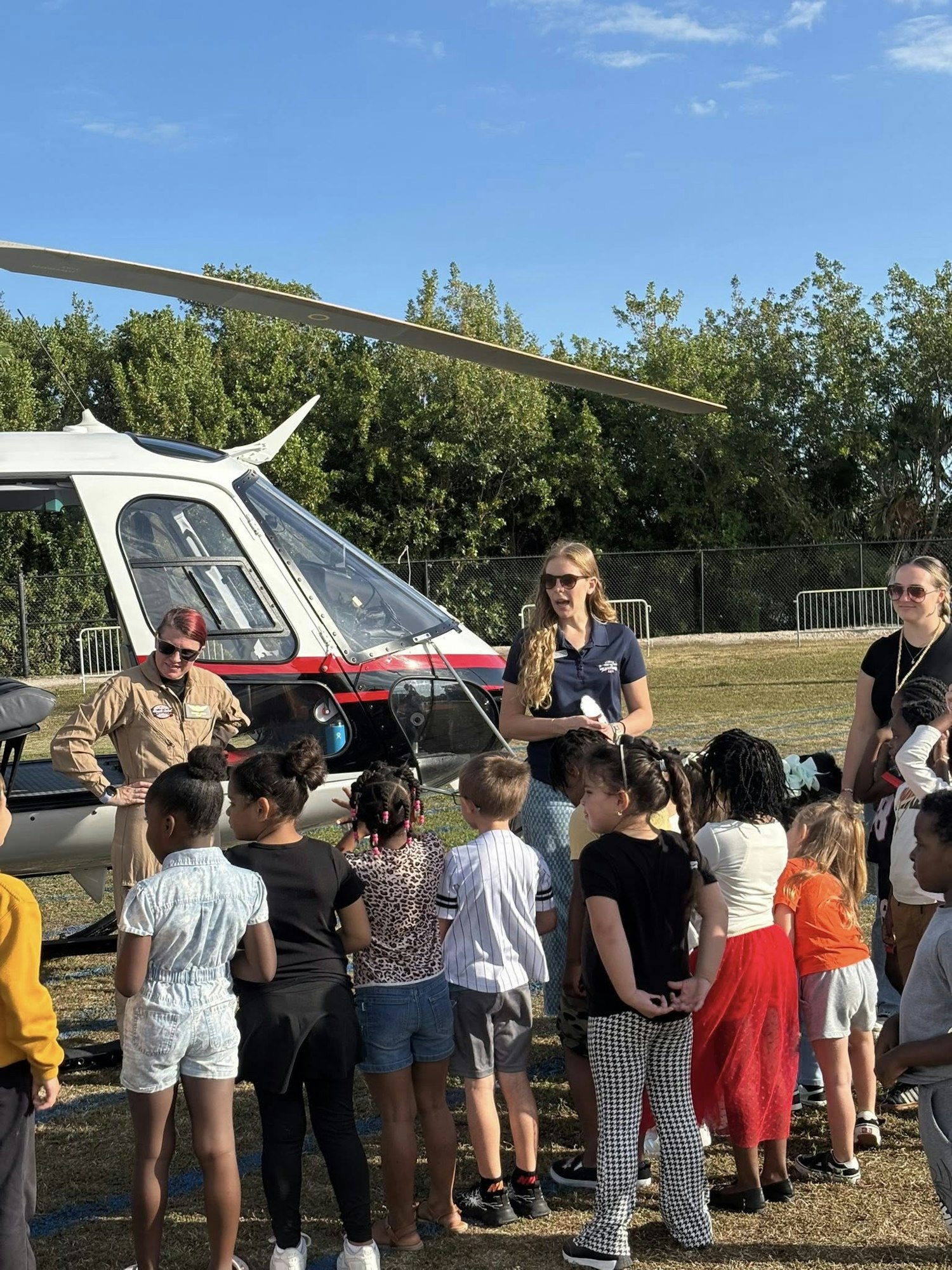 A group of children gathers around a helicopter, interacting with adults, likely learning about aviation.