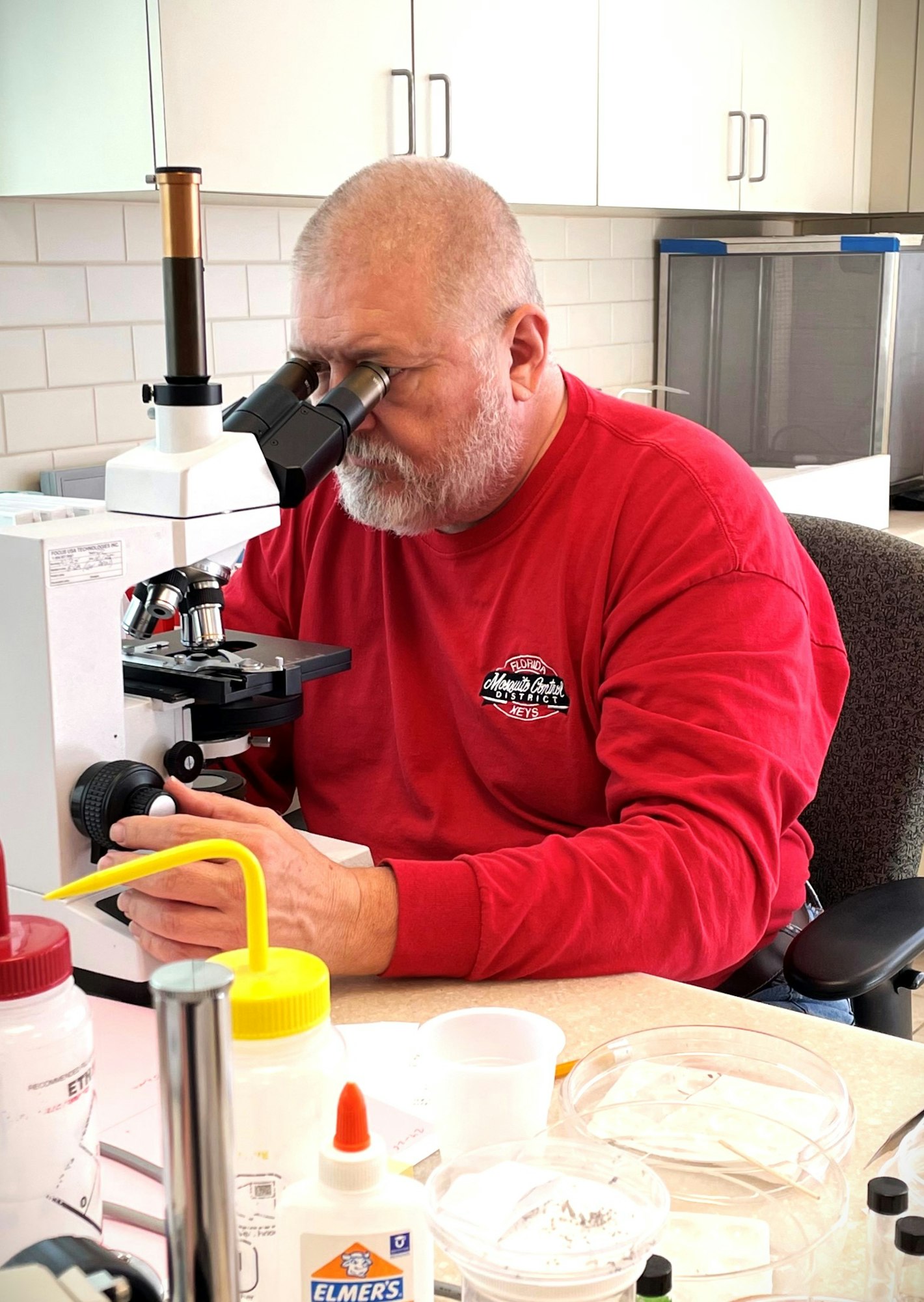A person using a microscope among various lab items.