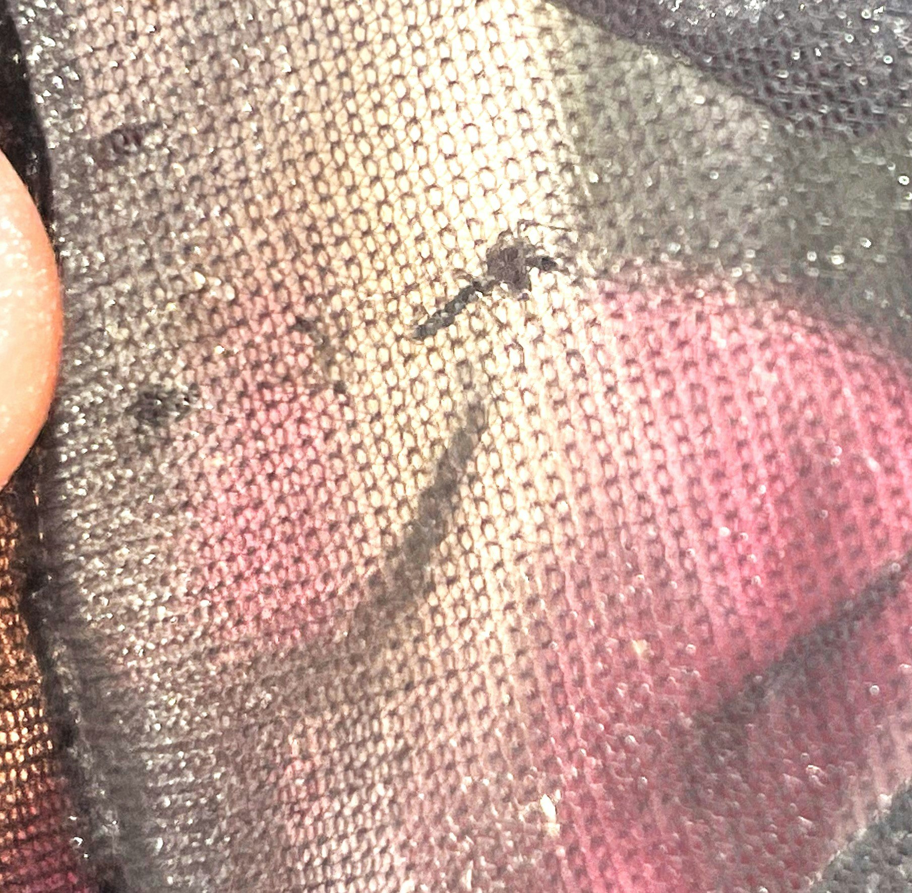 Close-up of a mesh fabric with a colorful background and a small tear.