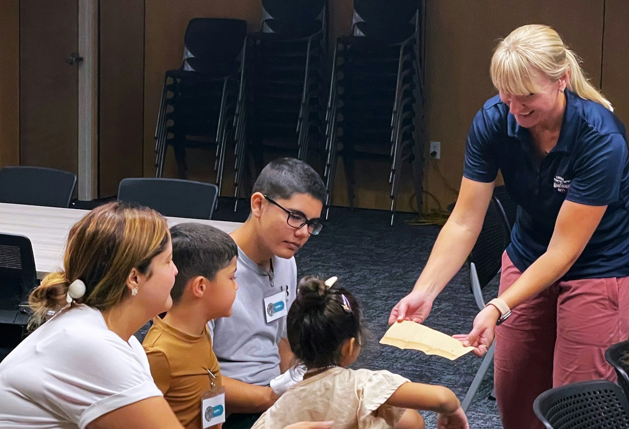 A group of people, including a child, engaged with a woman showing a paper.