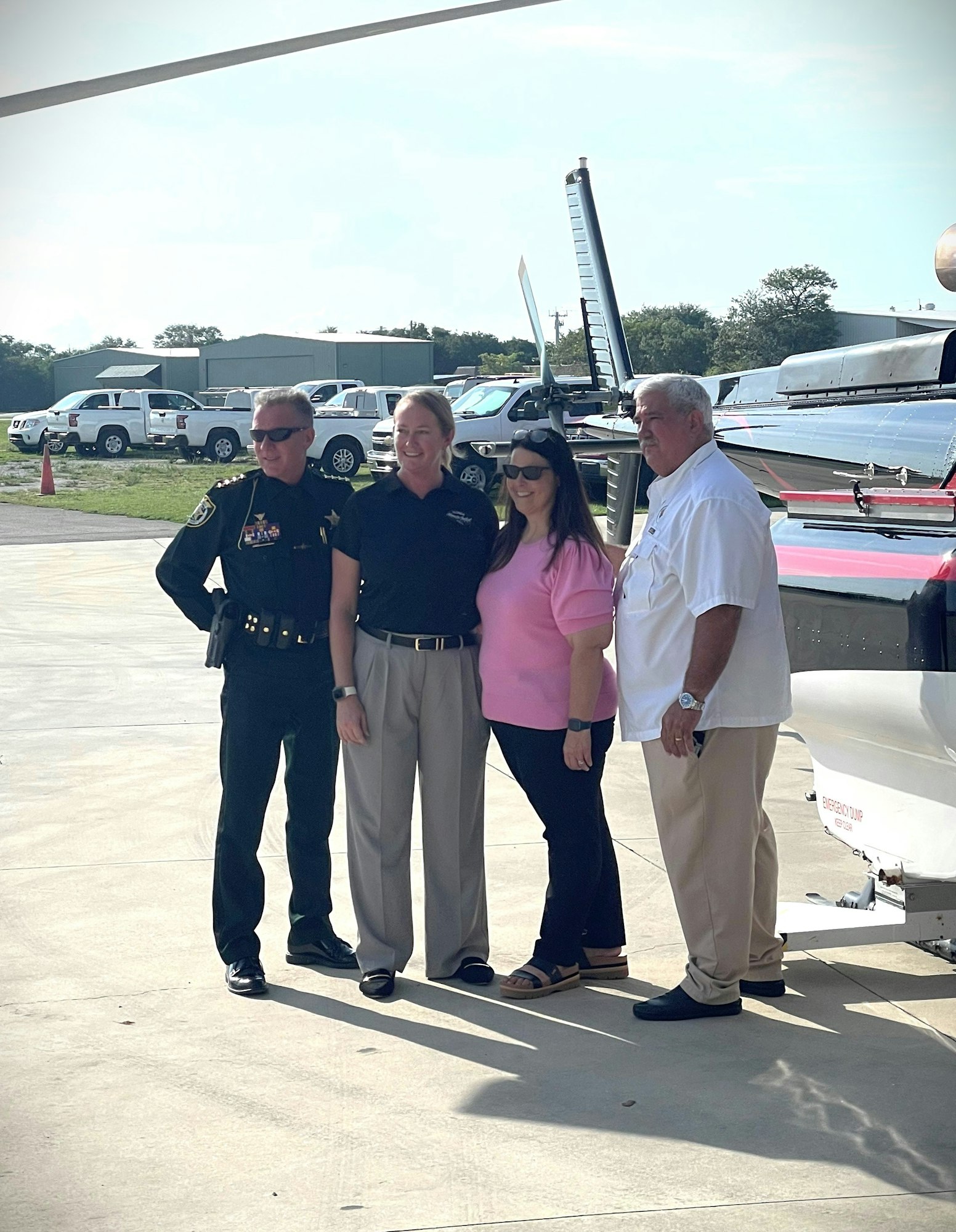Four individuals posing beside a helicopter, with one person in law enforcement uniform.