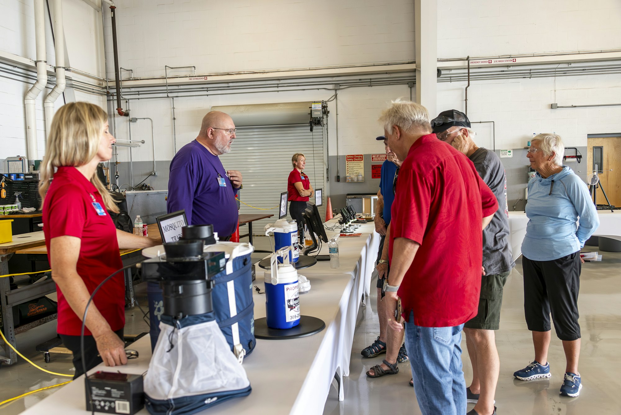People gathered at a table with mosquito traps and equipment on display in a workshop setting.
