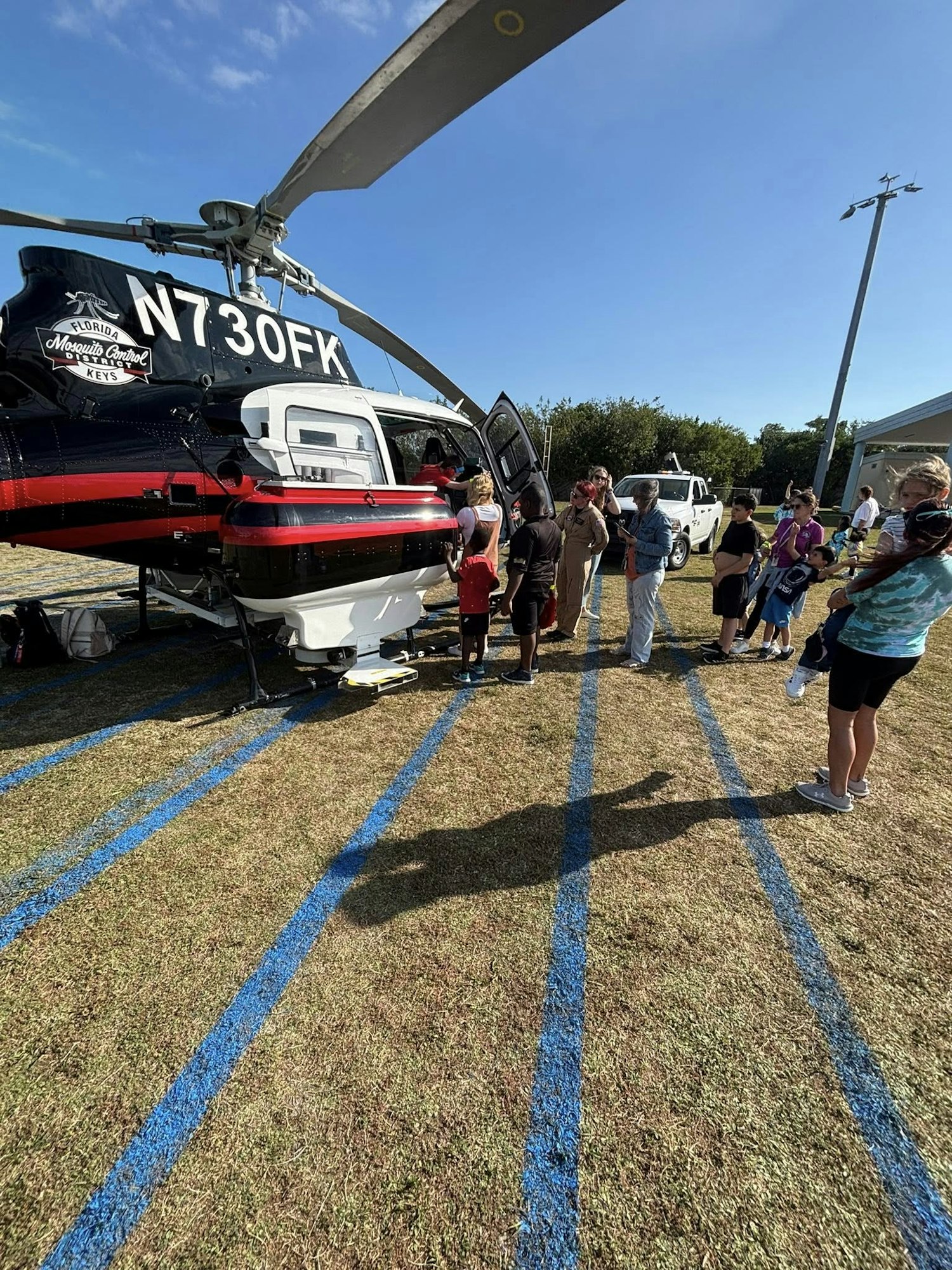 A helicopter on the ground with a group of people, including children, gathered around, likely for a demonstration or event.