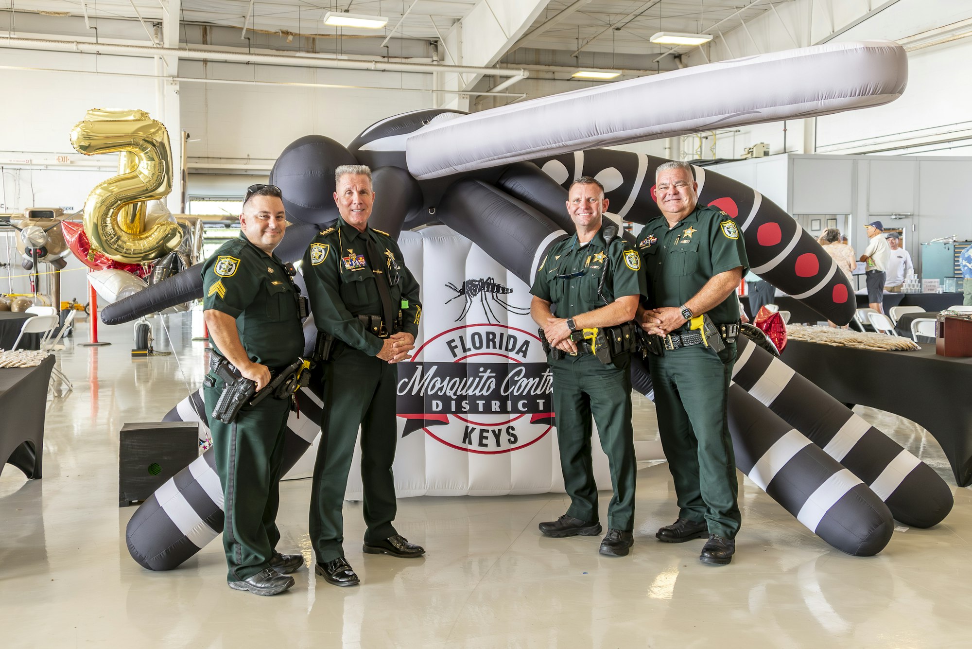 Four officers standing in front of a "Florida Keys Mosquito Control District" sign with a large inflatable mosquito.