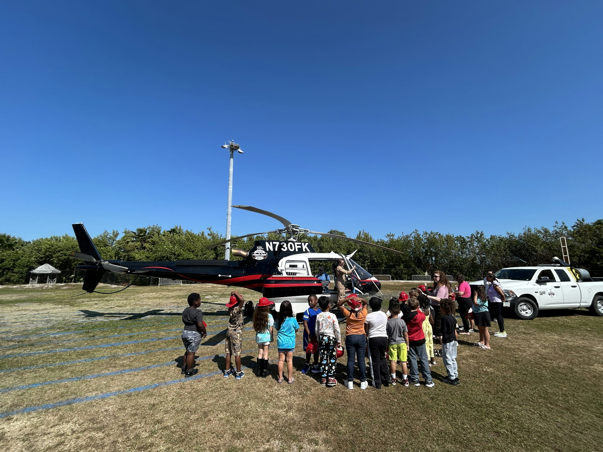 A group of children gathers around a helicopter on a sunny day, with a few adults present nearby.