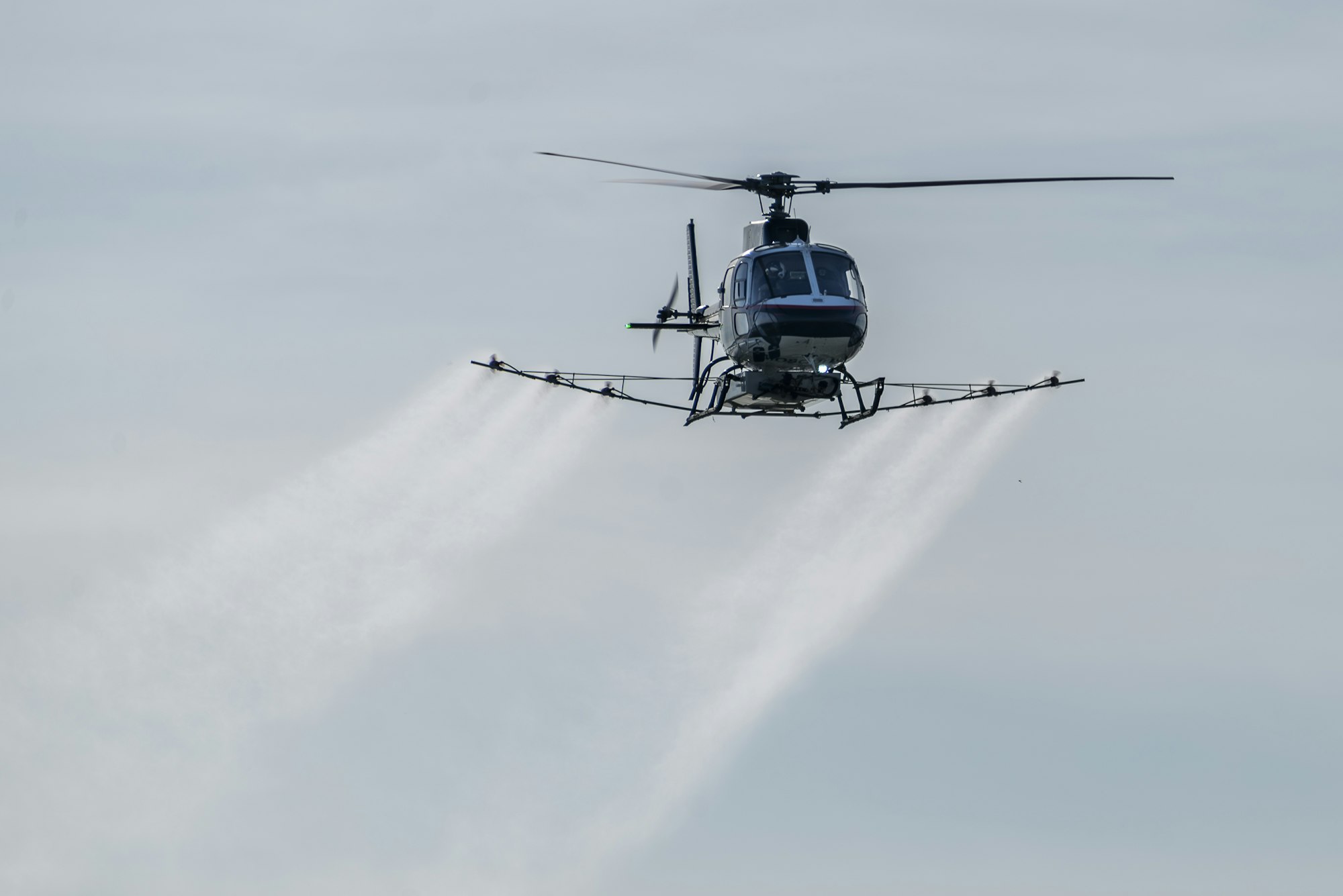 A helicopter spraying liquid into the sky from attached nozzles.