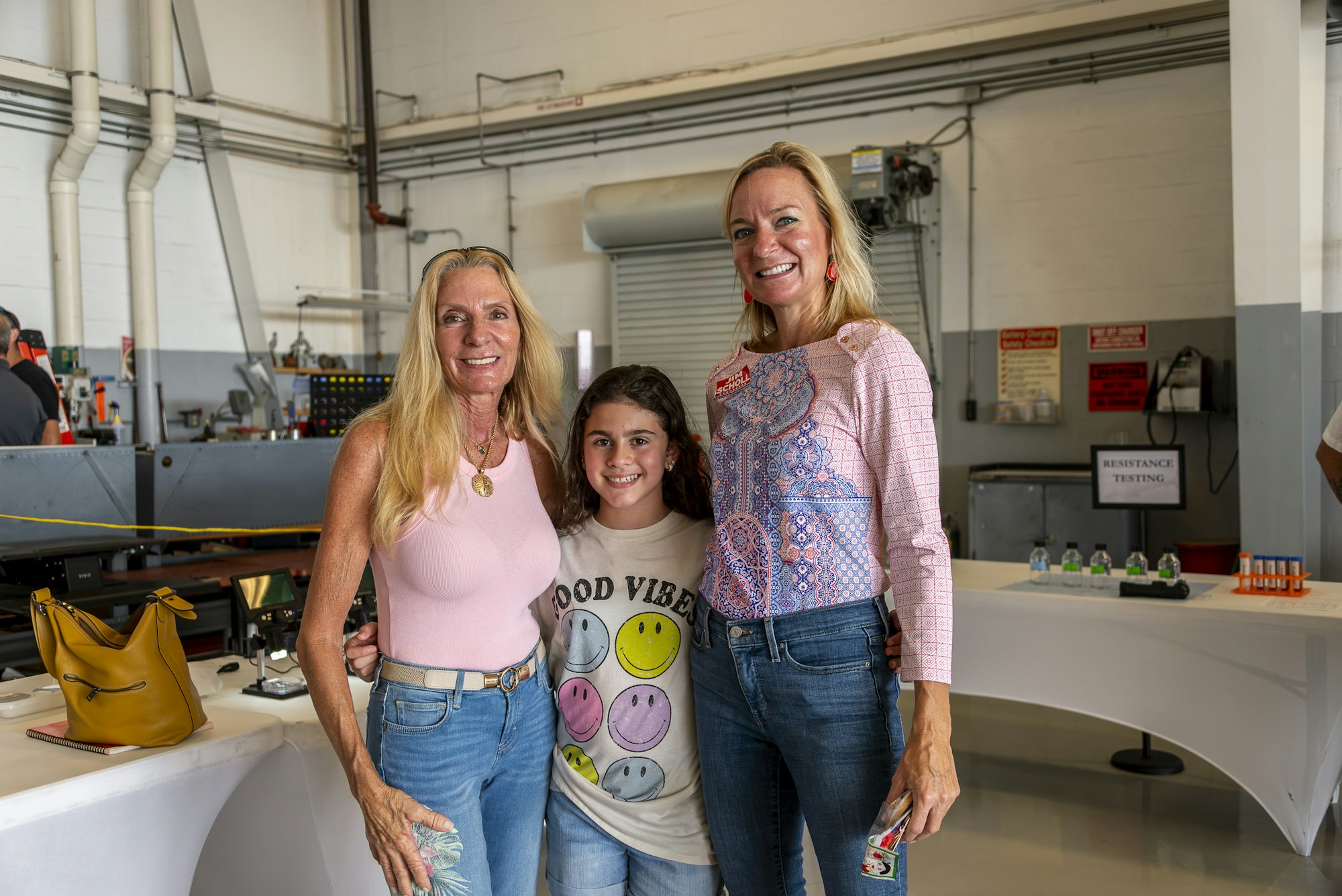 Three people smiling in a workshop setting with machines and testing equipment.