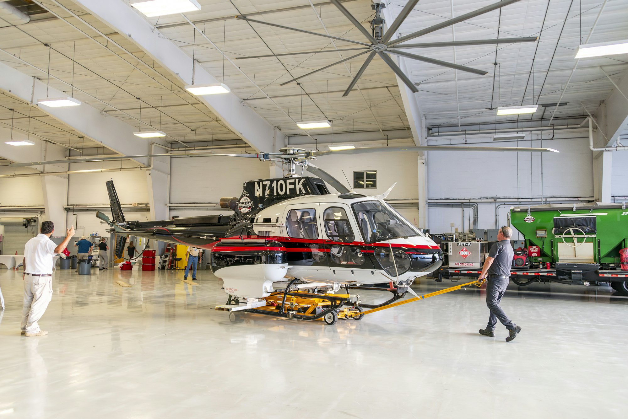 A helicopter being towed inside a spacious hangar by people.