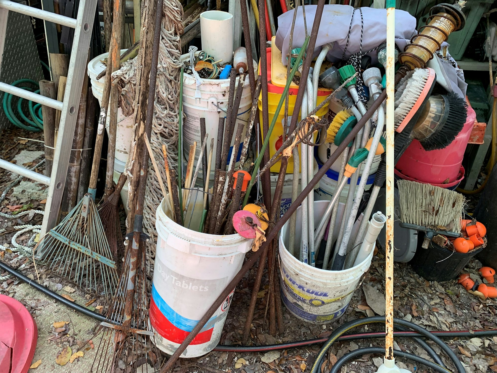 Buckets filled with assorted garden tools, rakes, hoses, and brushes piled together.