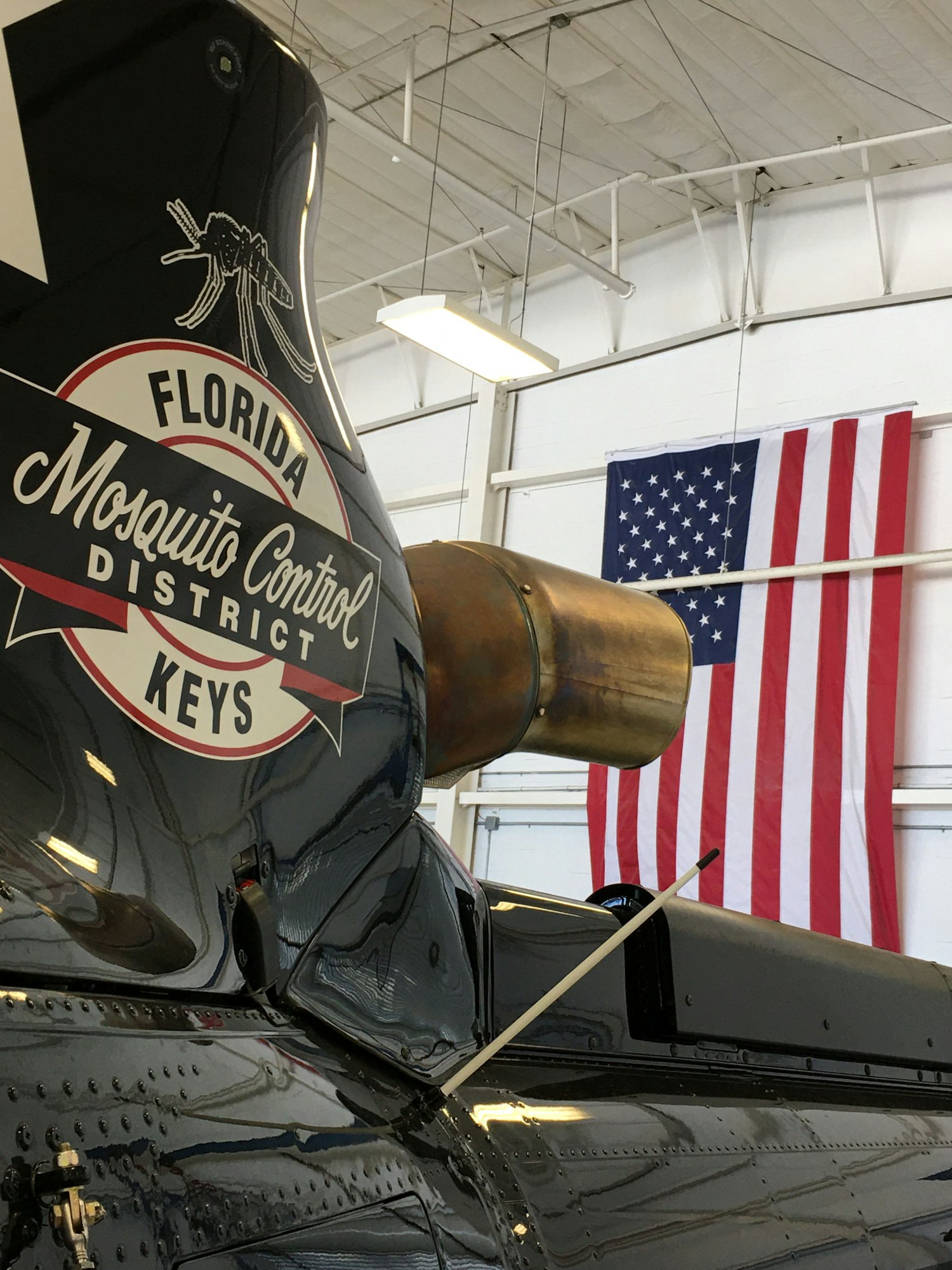 Helicopter tail with "Florida Mosquito Control District - KEYS" emblem, US flag in the background.