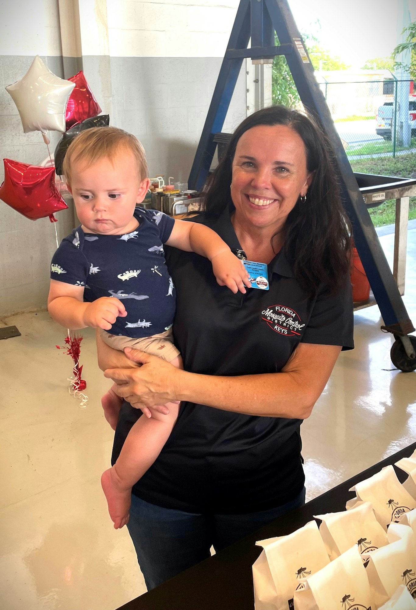 A woman holding a toddler with party balloons in the background.