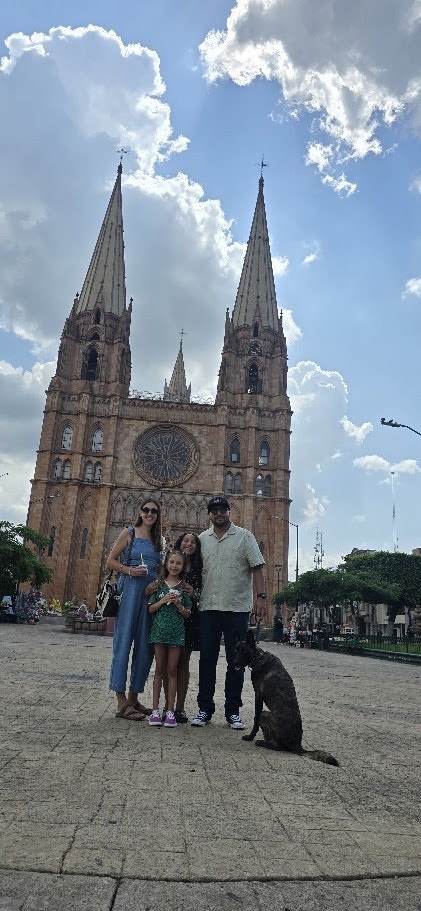 Julianna and her family poses with a dog in front of a stunning historic building with twin spires under a partly cloudy sky.