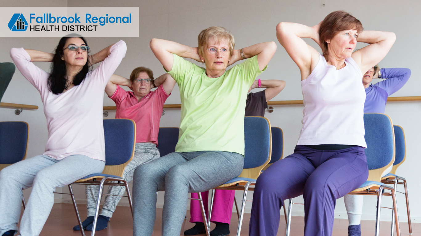 The image shows a group of women participating in a seated exercise class, focusing on stretching and wellness.