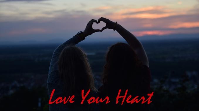 Two people are silhouetted against a sunset, making a heart shape with their hands. Text overlay reads "Love Your Heart."