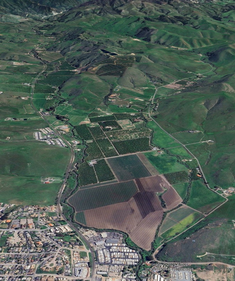 The image shows an aerial view of rolling green hills, vineyards, and residential areas, with agricultural land visible.