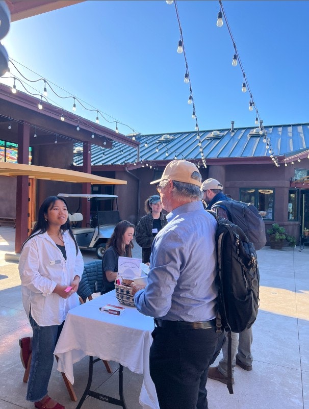 A sunny outdoor setting with people at a table, likely for an event. There’s a sign-up or information display.