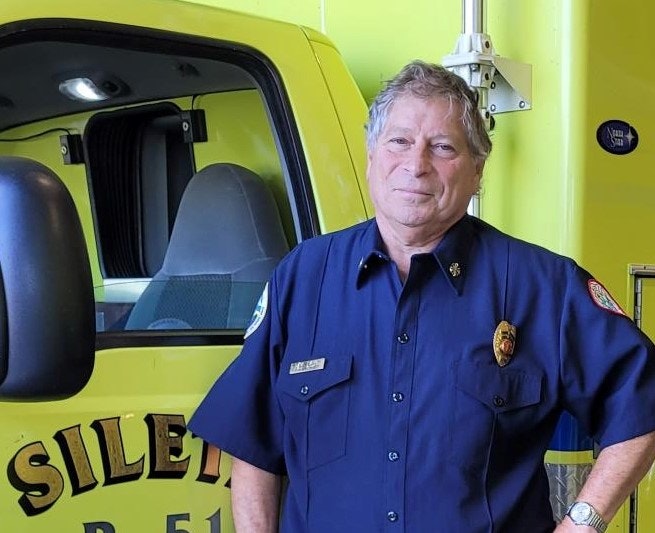 A firefighter in uniform standing in front of a yellow firetruck.