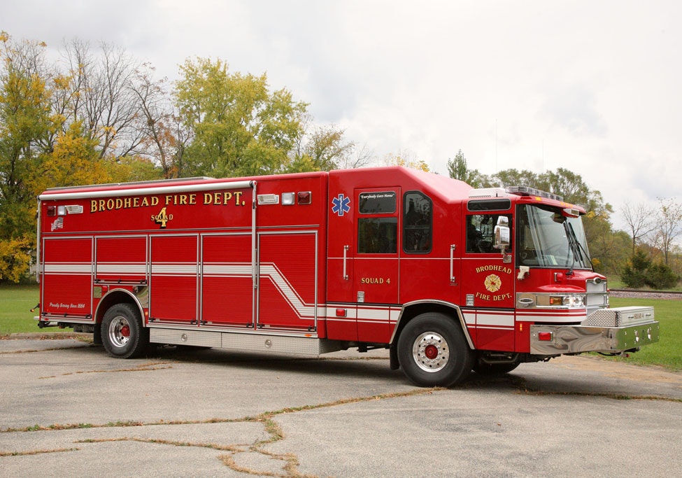 Red Brodhead Fire Department rescue vehicle on a driveway, clear sky, autumn foliage.