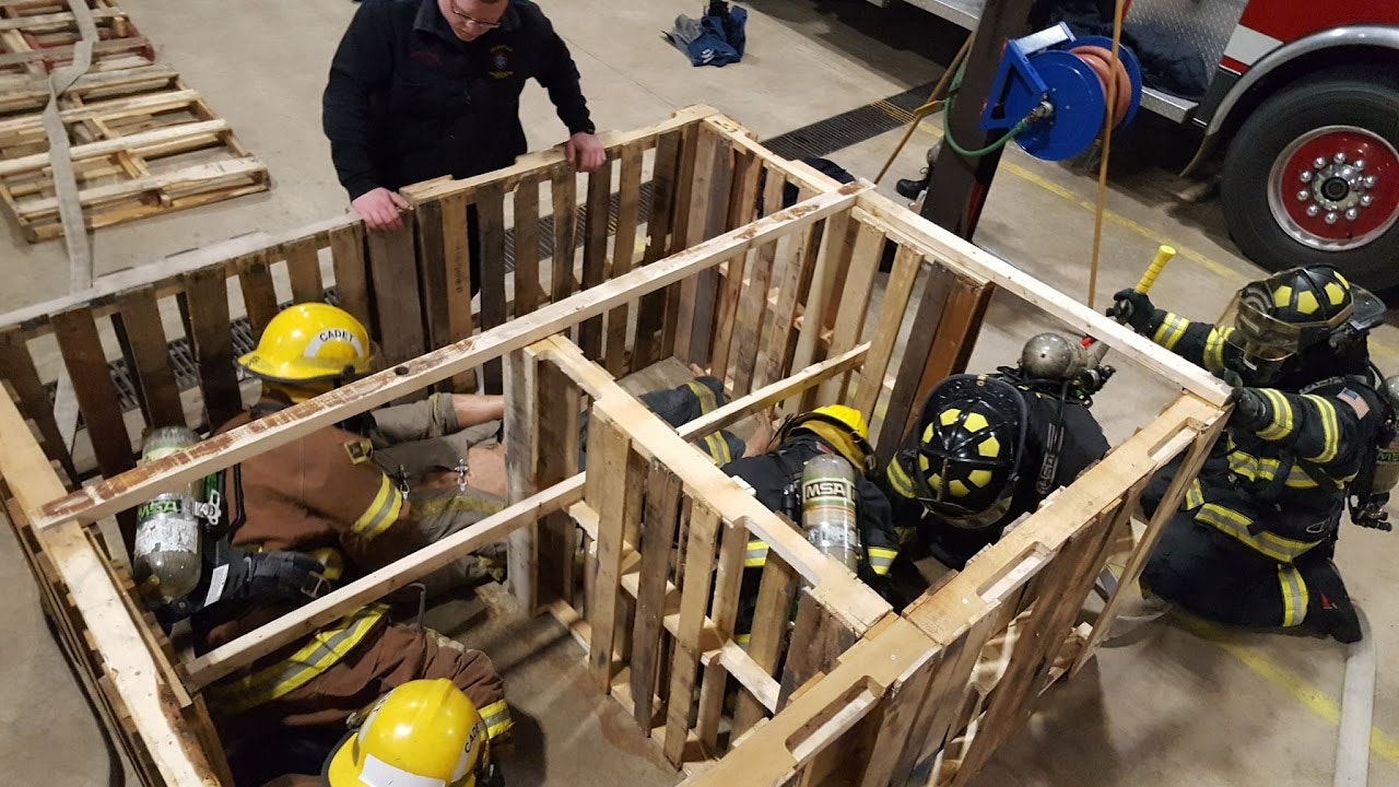 Firefighters training in a confined space simulation using wooden pallets.