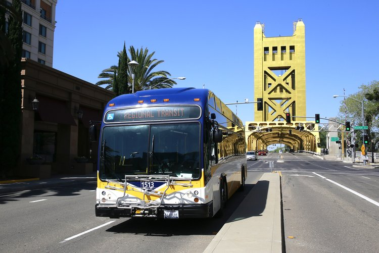 A city bus in front of a yellow bridge with palm trees and clear skies.