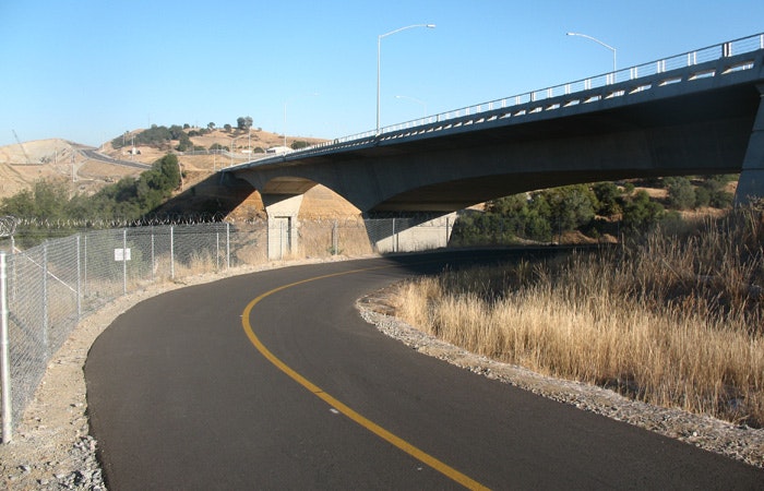 Curvy paved path leading to an overpass with dry grass and hills.