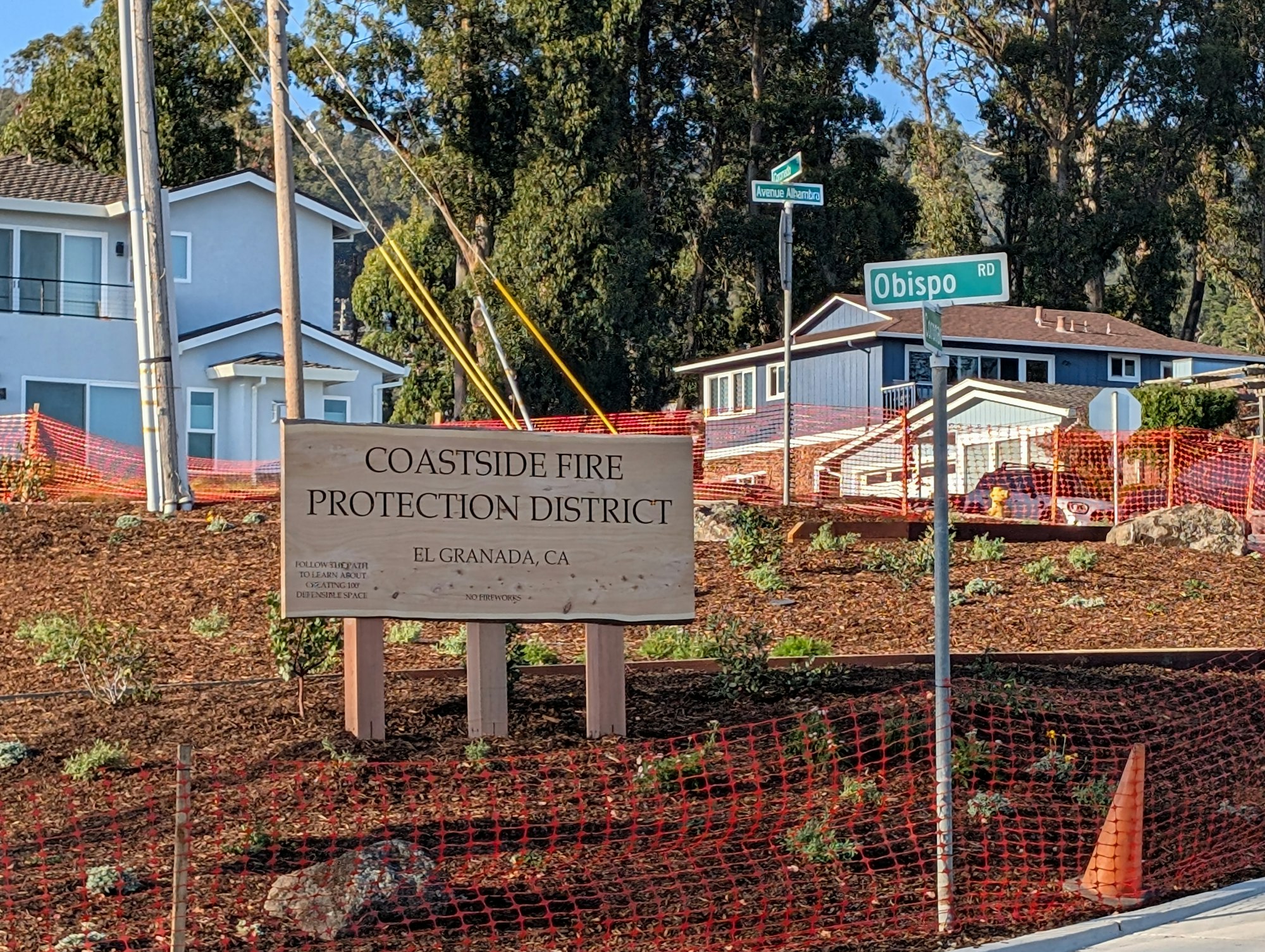 Sign for Coastside Fire Protection District in El Granada, CA, near a red fence and houses, with street signs for Obispo Rd and Avenue Alhambra.