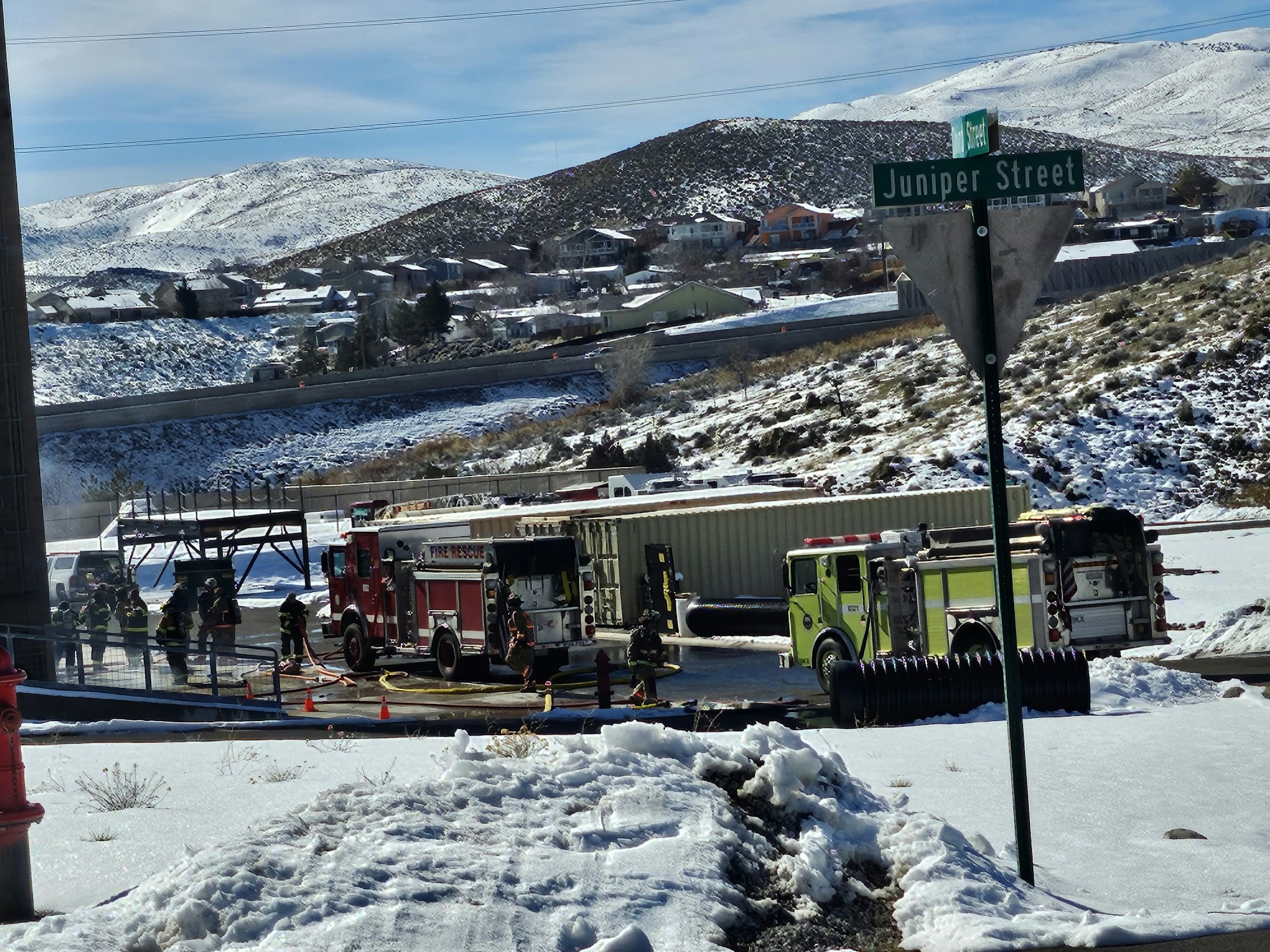 Emergency responders at a snowy scene with fire trucks and personnel, near Juniper Street, likely addressing an incident.