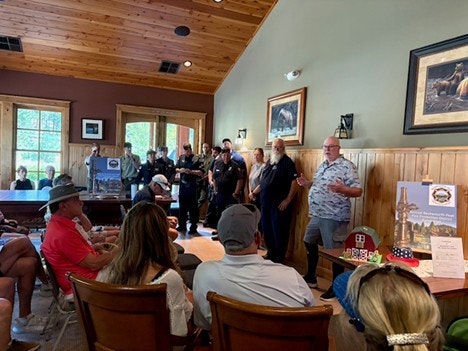 A meeting taking place indoors with people seated, while a few individuals stand and speak, likely discussing community matters.