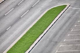 An overhead view of a curved road with a grassy median and empty parking spaces beside it.