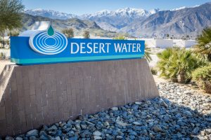 A sign for "Desert Water" set against a backdrop of mountains and palm trees, suggesting a utility or water service in a desert area.