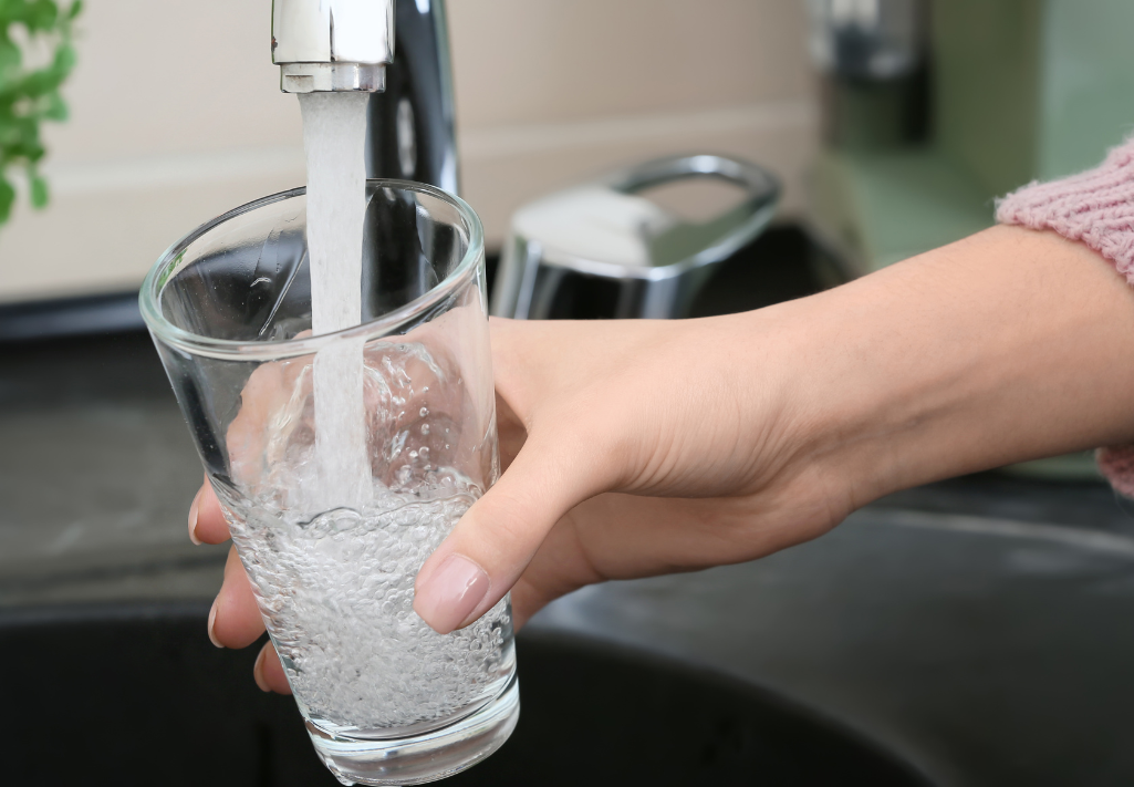 A hand pours water from a faucet into a glass, showcasing bubbling and fresh water being filled.