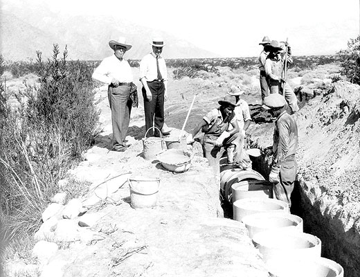 The image shows a group of men working on a construction site, possibly involved in digging or building with large circular elements.