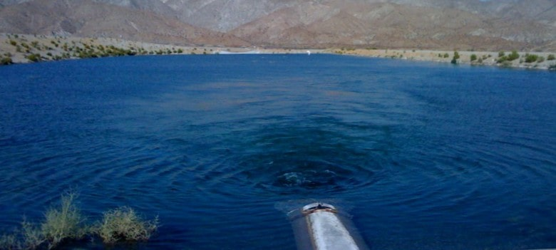 The image shows a body of water with a visible surface and some ripples, surrounded by rocky terrain and vegetation.